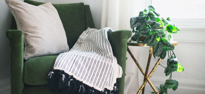 A green arm chair with a stripped throw blanket
