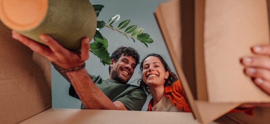 Young,Couple,Smiling,And,Unpacking,Belongings,From,Cardboard,Boxes,,Enjoying
