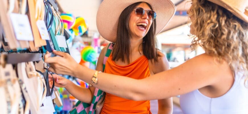 Two smiling women in summer hats shopping for sandals